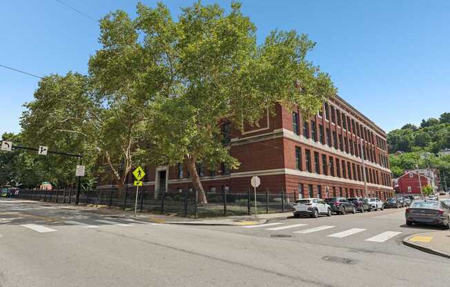 A street view with a red brick building, cars, and trees.