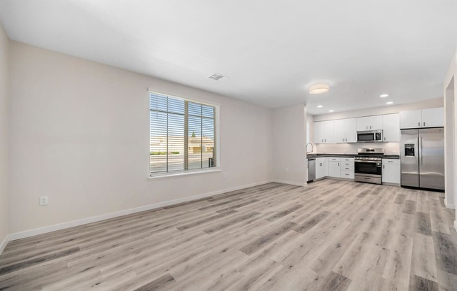 an empty living room and kitchen with wood flooring and a window