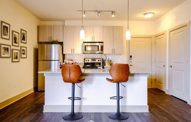 a photo of a kitchen island with bar stools and kitchen in the background
