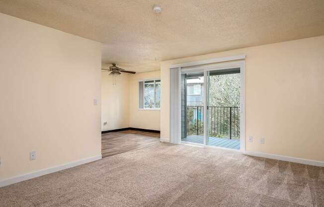 A spacious room with a ceiling fan and sliding glass doors leading to a balcony.