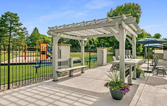 A white pergola is over a patio with a table and chairs.