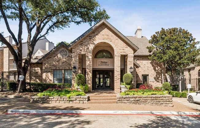 A building with a stone facade and a sign that reads "Ladies' Manor" is surrounded by trees and flowers.