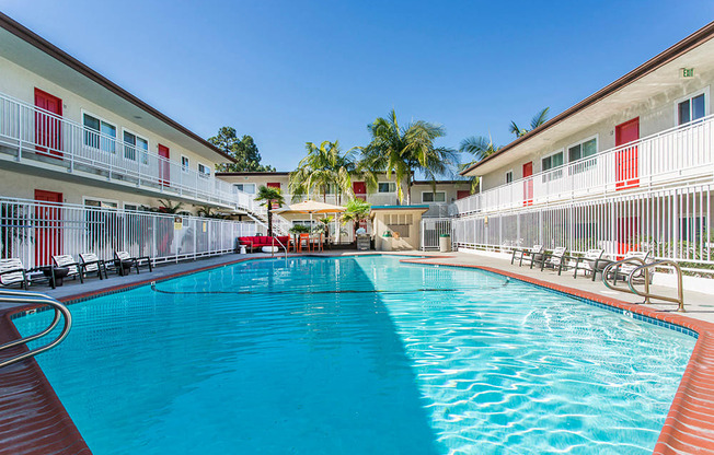 Outdoor swimming pool with sun chairs, a lounge area lined with apartments, and palm trees at Pacific Sands, San Diego, CA