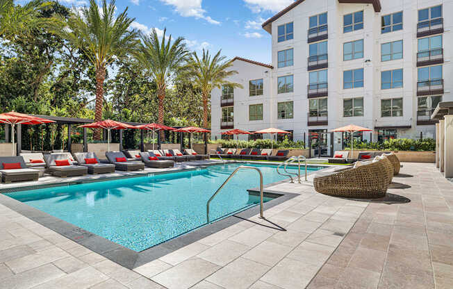 Resort-style swimming pool with cushioned loungers, vibrant umbrellas, and palm trees for a true vacation vibe