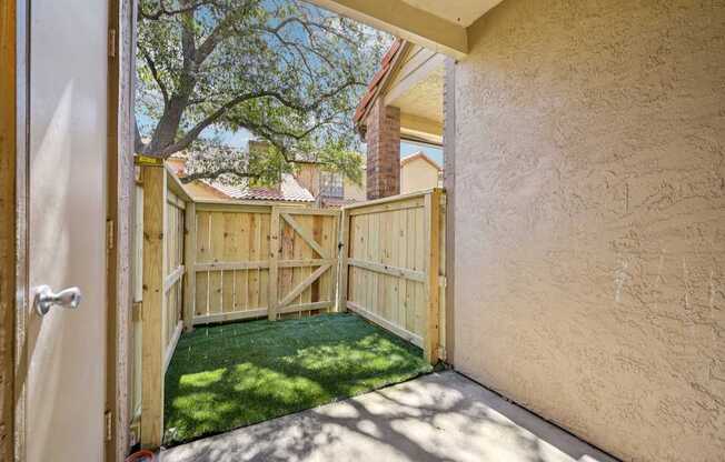 A wooden gate opens to a backyard with a green lawn.