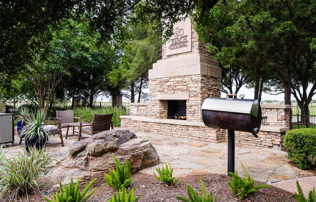 A stone fireplace with a mailbox on top is surrounded by green plants.