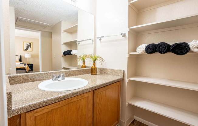 A bathroom with a sink, mirror, and shelves with towels.
