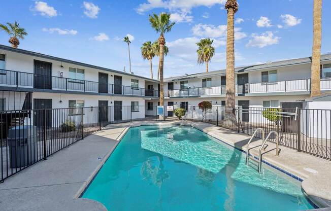 A swimming pool in front of a building with palm trees.