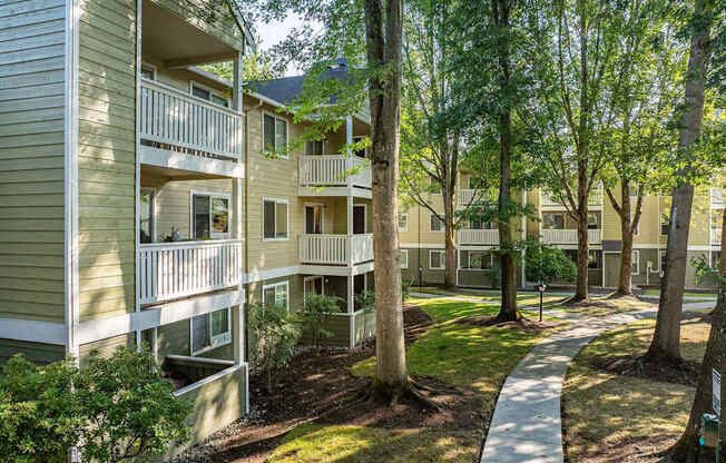 Apartment complex with green trees and a walkway.