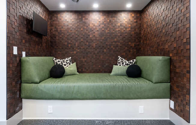 A green couch with two pillows sits against a brick wall.