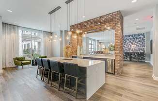 A kitchen with a brick wall and a long island with chairs.