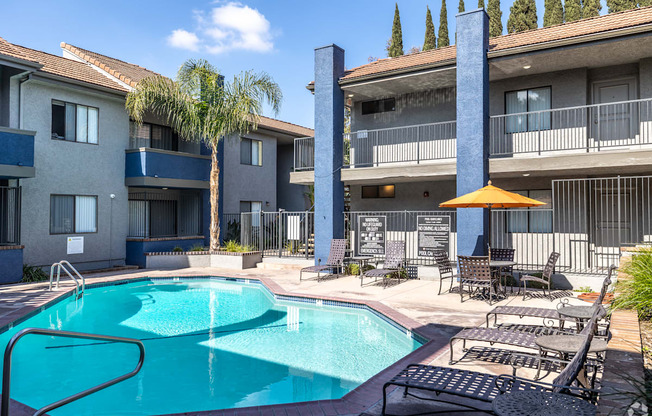 A swimming pool surrounded by chairs and umbrellas in front of apartment buildings.