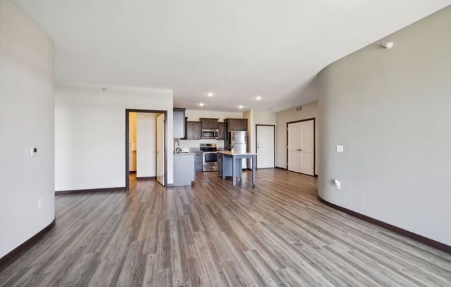 an empty living room and kitchen with wood floors and white walls