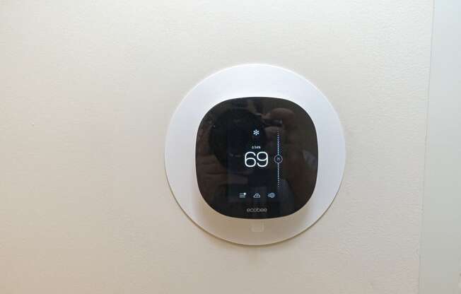 a digital thermostat on a wall with a person taking a picture of themselves