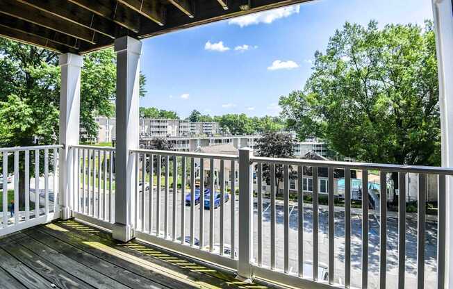 A white railing on a wooden deck overlooks a parking lot.