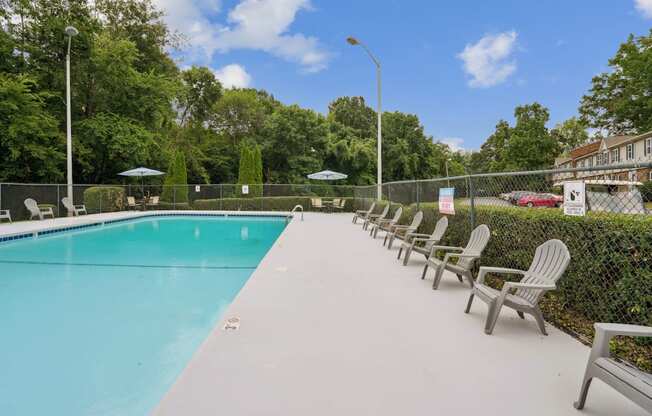 A pool surrounded by trees and chairs.