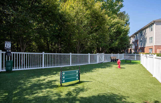 A white fence surrounds a green lawn with a bench and a fire hydrant.