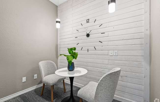 a small table with two chairs in front of a wall with a clock on it