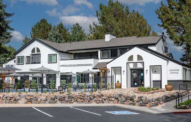 A white building with a black roof and a sign that says "Leasing Office" is in front of some trees.