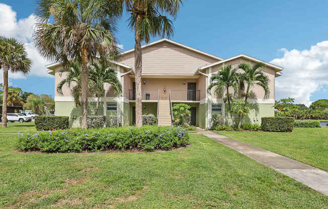 A house with a green lawn and palm trees in front.