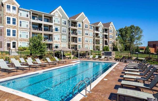 a swimming pool with lounge chairs in front of an apartment building
