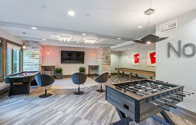 A foosball table is in the middle of a room with a pool table and a couch.