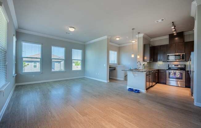 Living room with hardwood flooring facing kitchen with stainless steel appliances