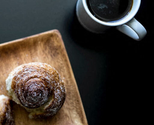 a doughnut sitting on top of a wooden cutting board next to a cup of coffee
