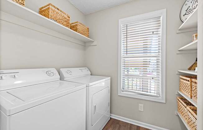 A laundry room with a washer and dryer and a window with blinds.