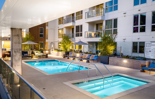 Apartments In DTLA For Rent - Emerald - An Outdoor Pool Area With Hot Tub And Lounge Seating At The Base Of An Apartment Tower