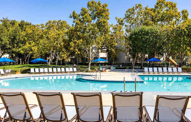A pool surrounded by trees and chairs.