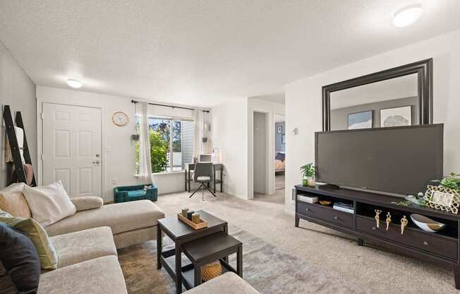 A living room with a couch, a coffee table, flat screen TV, and a large mirror at Clackamas Trails Apartments, Oregon, 97222