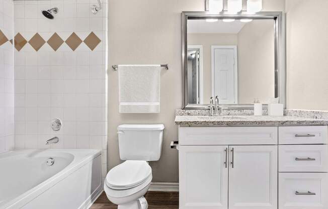 A white bathroom with a marble counter top and a large mirror.