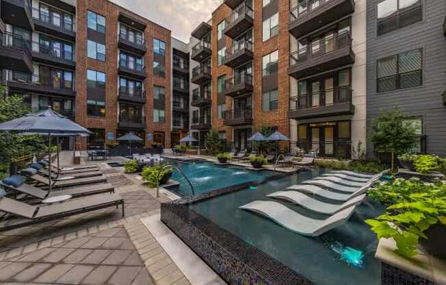 A pool surrounded by lounge chairs and umbrellas in a courtyard.