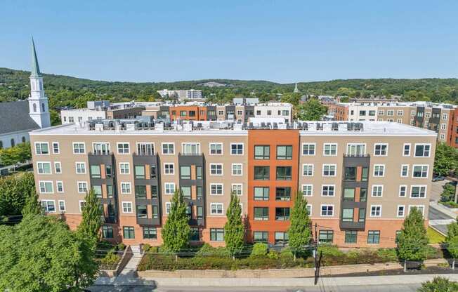 an aerial view of an apartment building with a church in the background at The Merc, Waltham, 02453