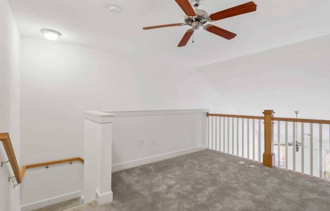 an empty living room with a ceiling fan and a staircase