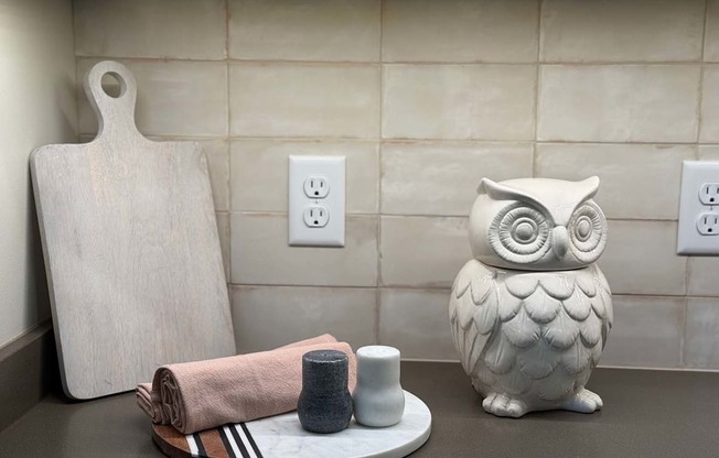 a kitchen countertop decorated with a wooden cutting board, and owl statue, and a serving tray