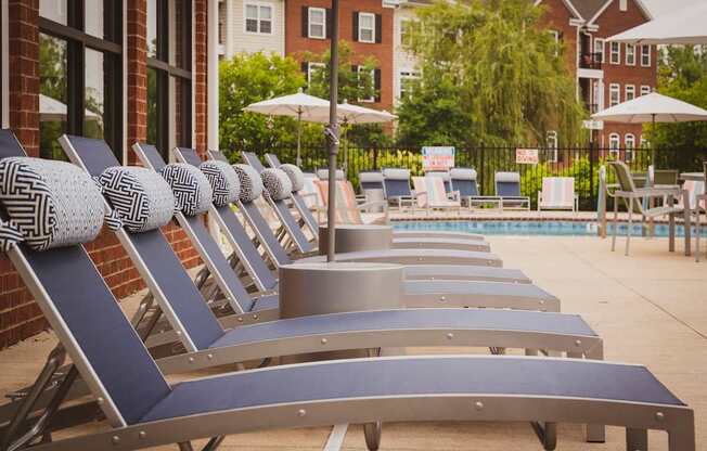 A row of sun loungers are lined up by a pool.