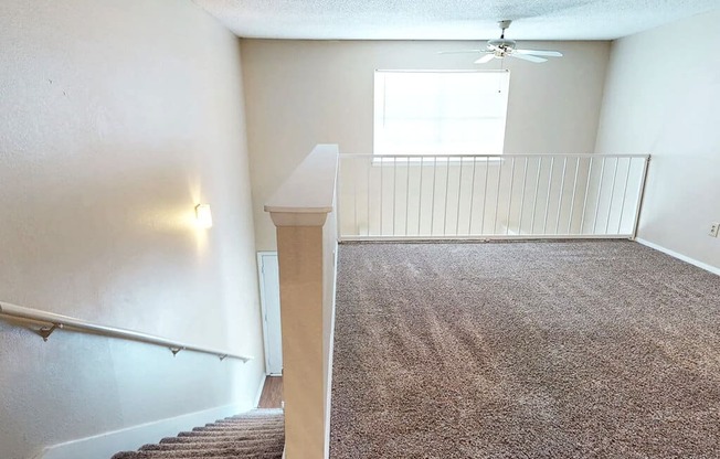 A room with a carpeted floor and a staircase leading to another room.