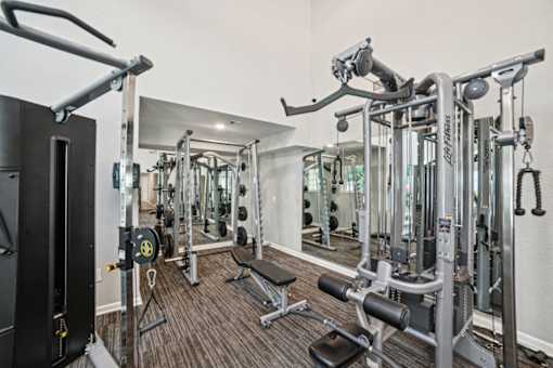 A gym with a variety of equipment including a squat rack, a leg press machine, and a cable machine.