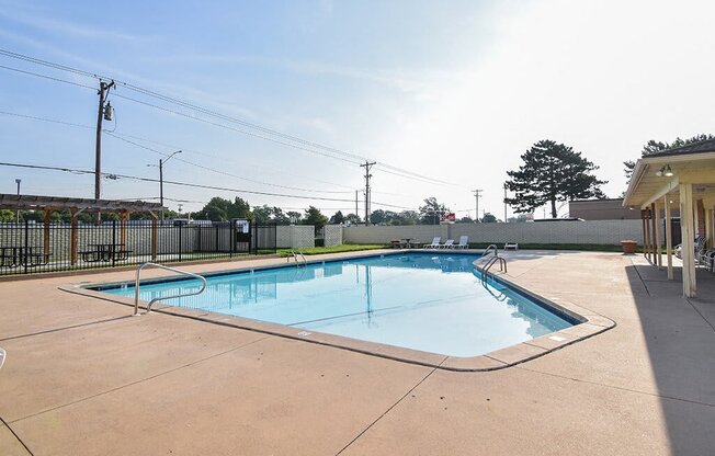 A large outdoor swimming pool with a concrete deck and a fence surrounding it.