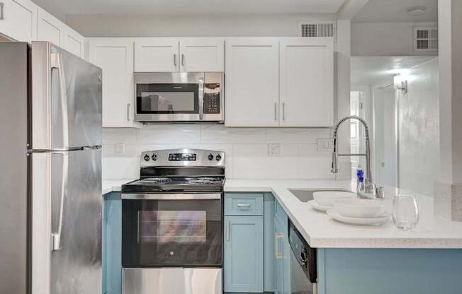 A kitchen with a stainless steel refrigerator, a black stove, and white cabinets.
