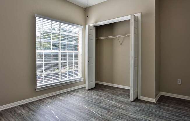 A room with a wooden floor and a large window with blinds.