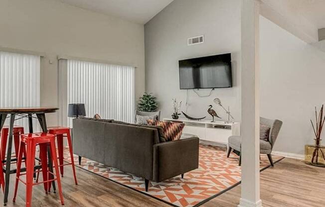 A living room with a grey couch, a television, and a wooden floor.