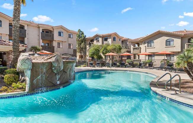 A swimming pool with a waterfall feature in front of apartment buildings.