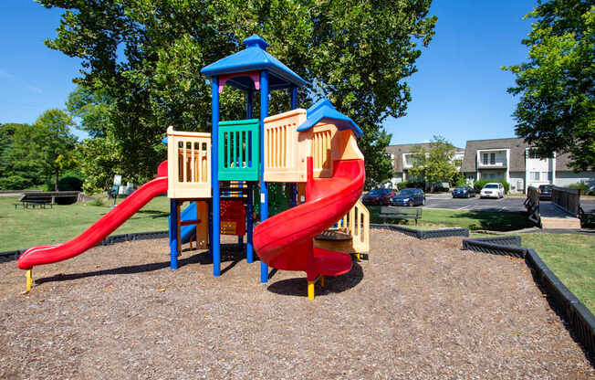 A playground with a red slide and a blue and yellow playhouse.