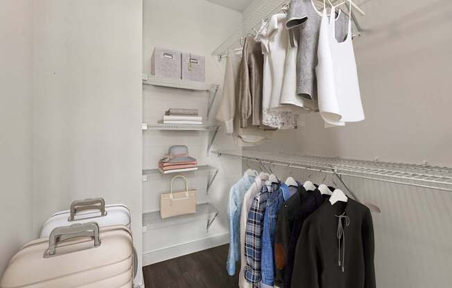 A suitcase is on the floor next to a closet with clothes hanging.