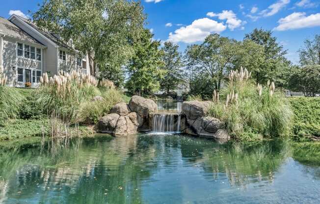 a pond with a waterfall in front of a house