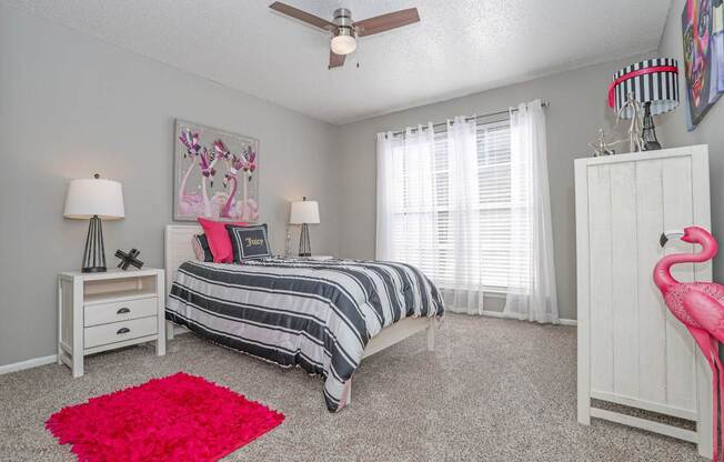 Model bedroom with a bed, nightstands, and a pink rug at Maplewood apartments in Shreveport, LA.