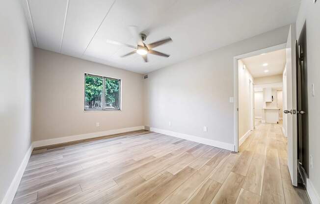 A room with a ceiling fan and a window with a view of trees.